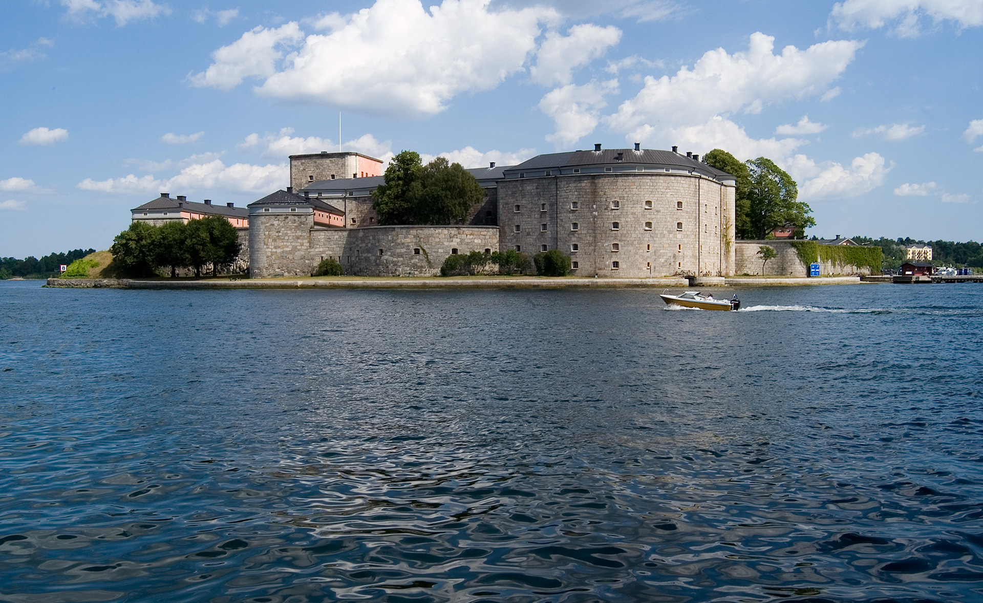 Runda hus står på en ö i vattnet. En båt åker förbi.