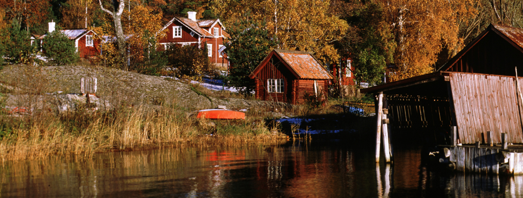 Små hus som står på en kulle. Kullen ligger intill vattnet.