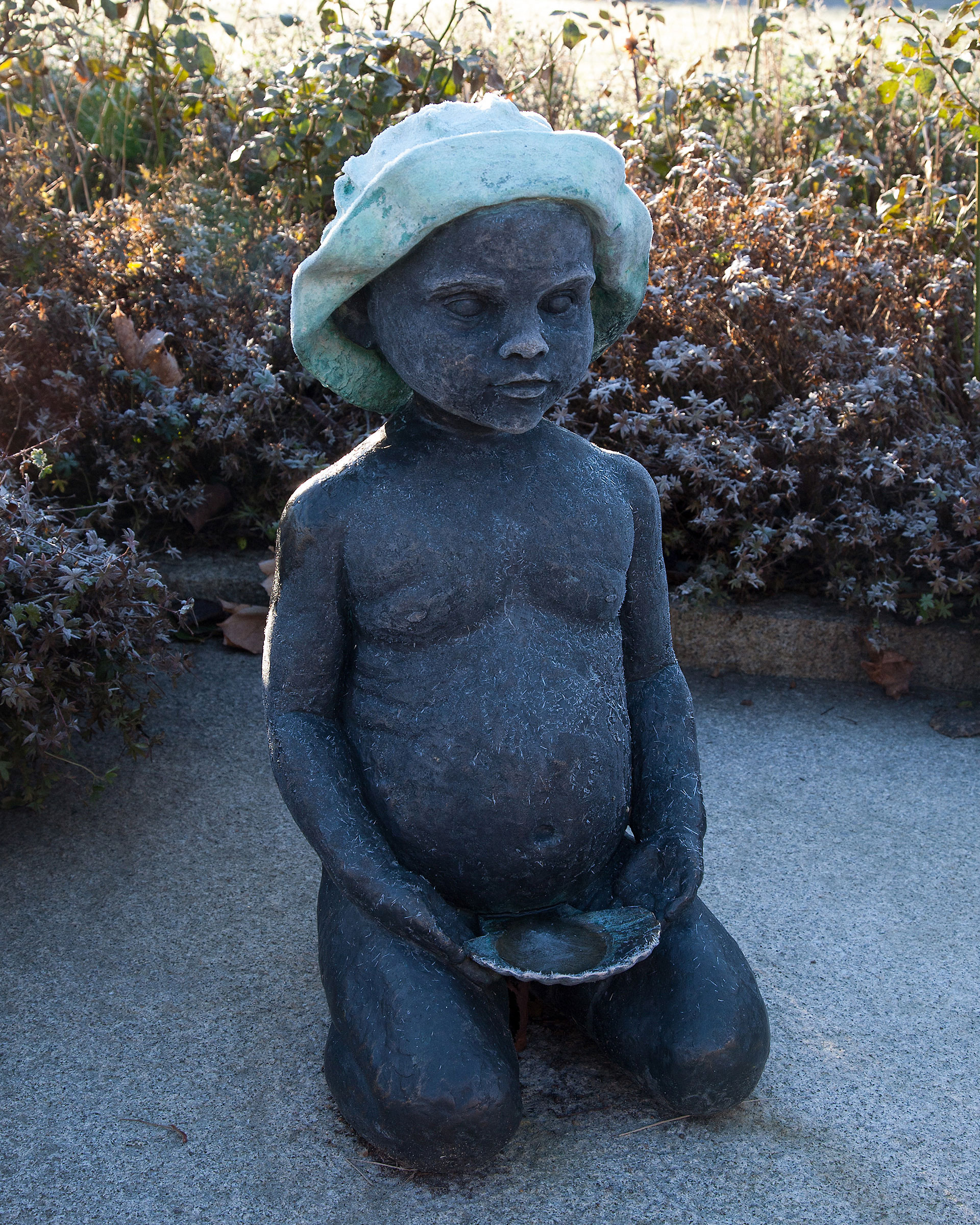 En skulptur av ett naket barn sitter på marken med en snäcka i händerna.