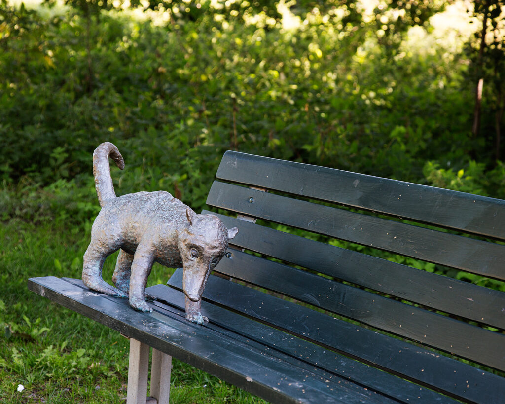 En näsbjörn gjord av sten står på en parkbänk.