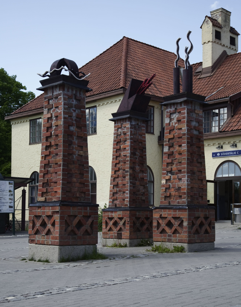 Tre skulpturer av tegel framför en gul byggnad.