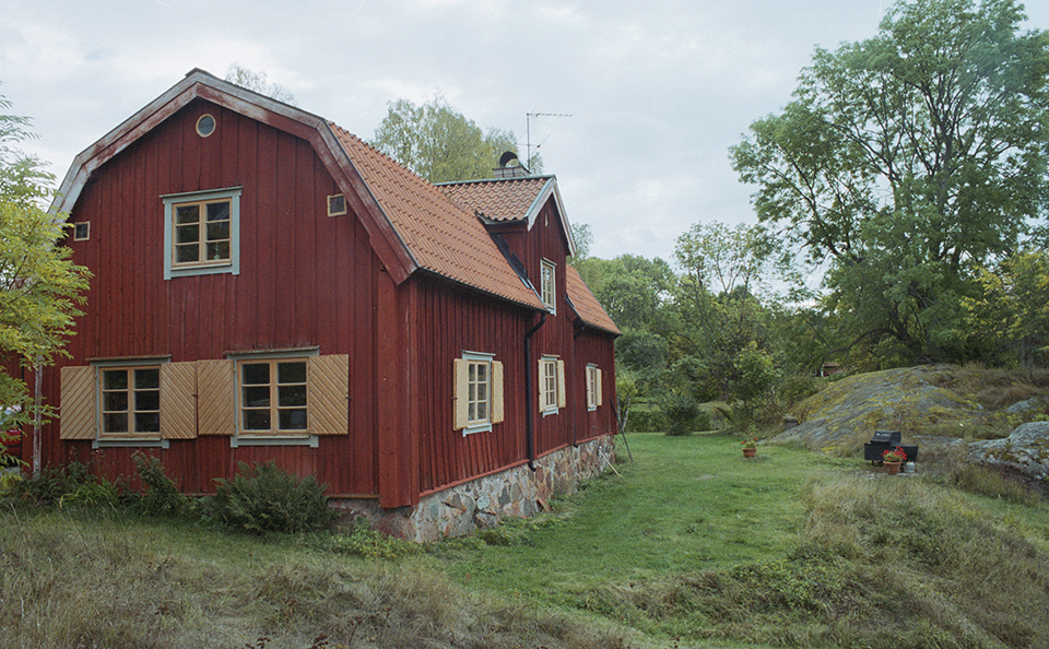 Ett trähus som står i en grönskande trädgård.