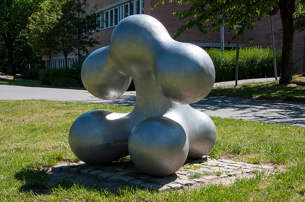 En abstrakt skulptur av en bubblig figur med armar och ben som sitter i gräset.