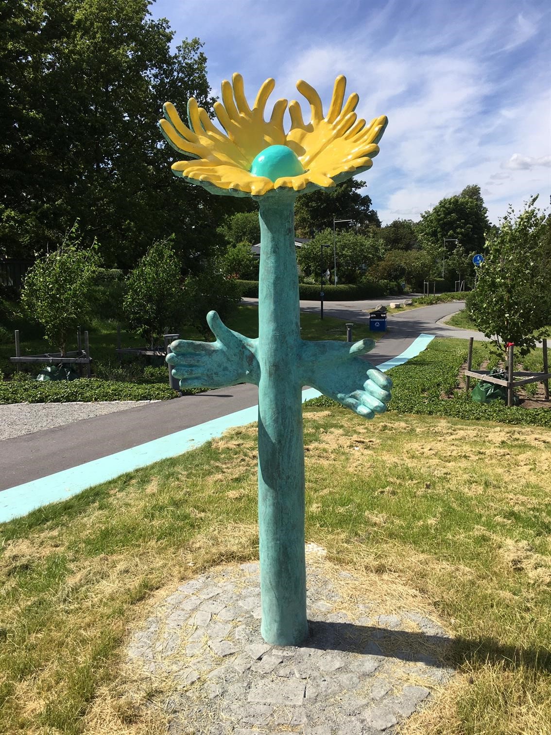 En skulptur av en stor gul blomma med grön stam välkomnar med öppna händer.