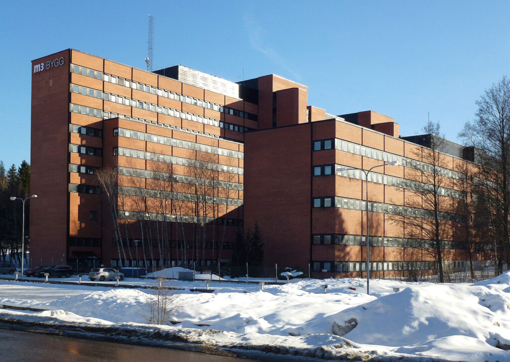 Stor kontorsbyggnad med olika tre olika höjder, 5-9 våningar hög. Byggd med rött tegel.