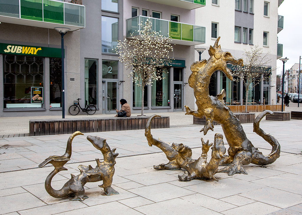 Skulptur med tre guldglänsande drakar på ett torg.