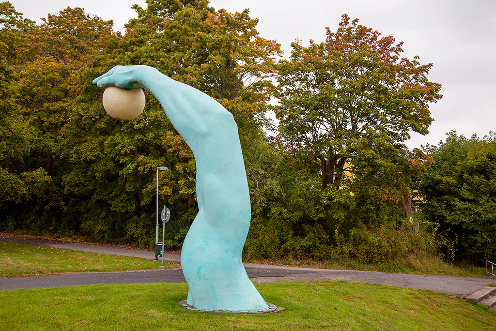 En skulptur av en fem meter hög turkos muskulös arm med en hand som håller i en rund lampa.