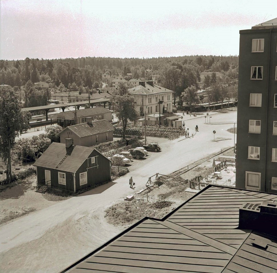 Svartvitt foto av stationen och några andra hus ur fågelperspektiv.