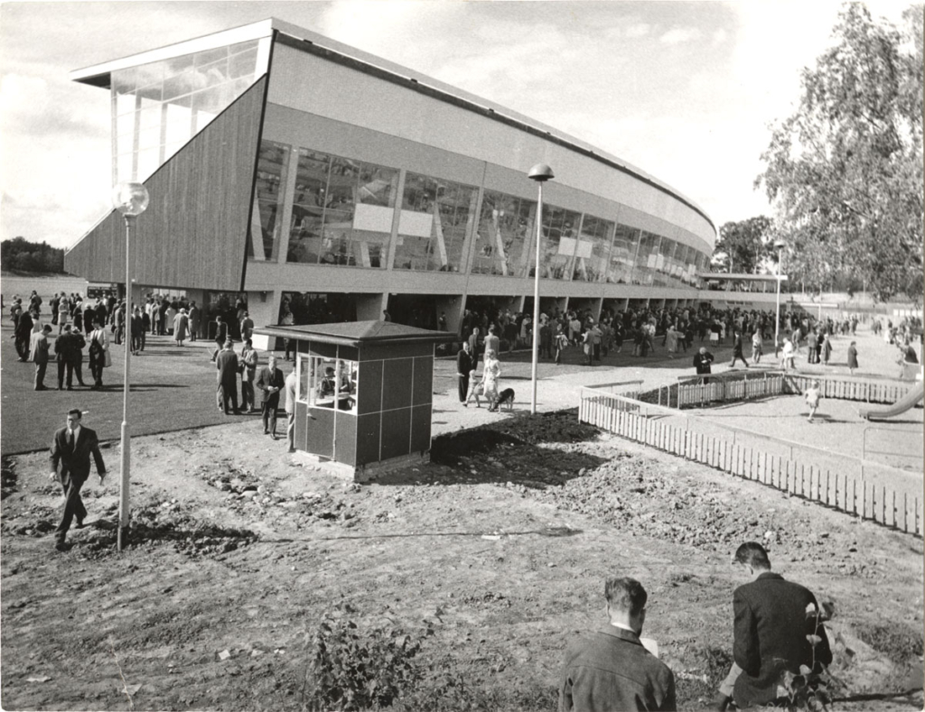 Svartvitt foto. Galoppläktare med publik utanför.